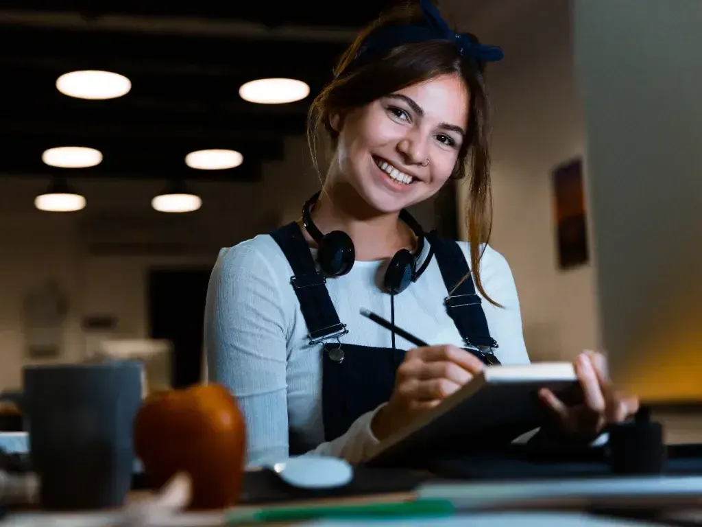 Mulher sorri enquanto trabalha em um notebook, sentada em um ambiente de café.