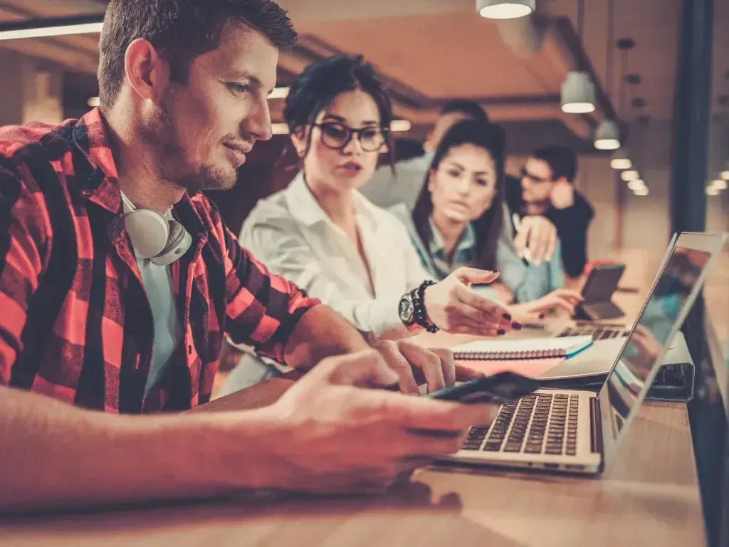 Grupo de colegas reunido ao redor de um notebook em sala iluminada.