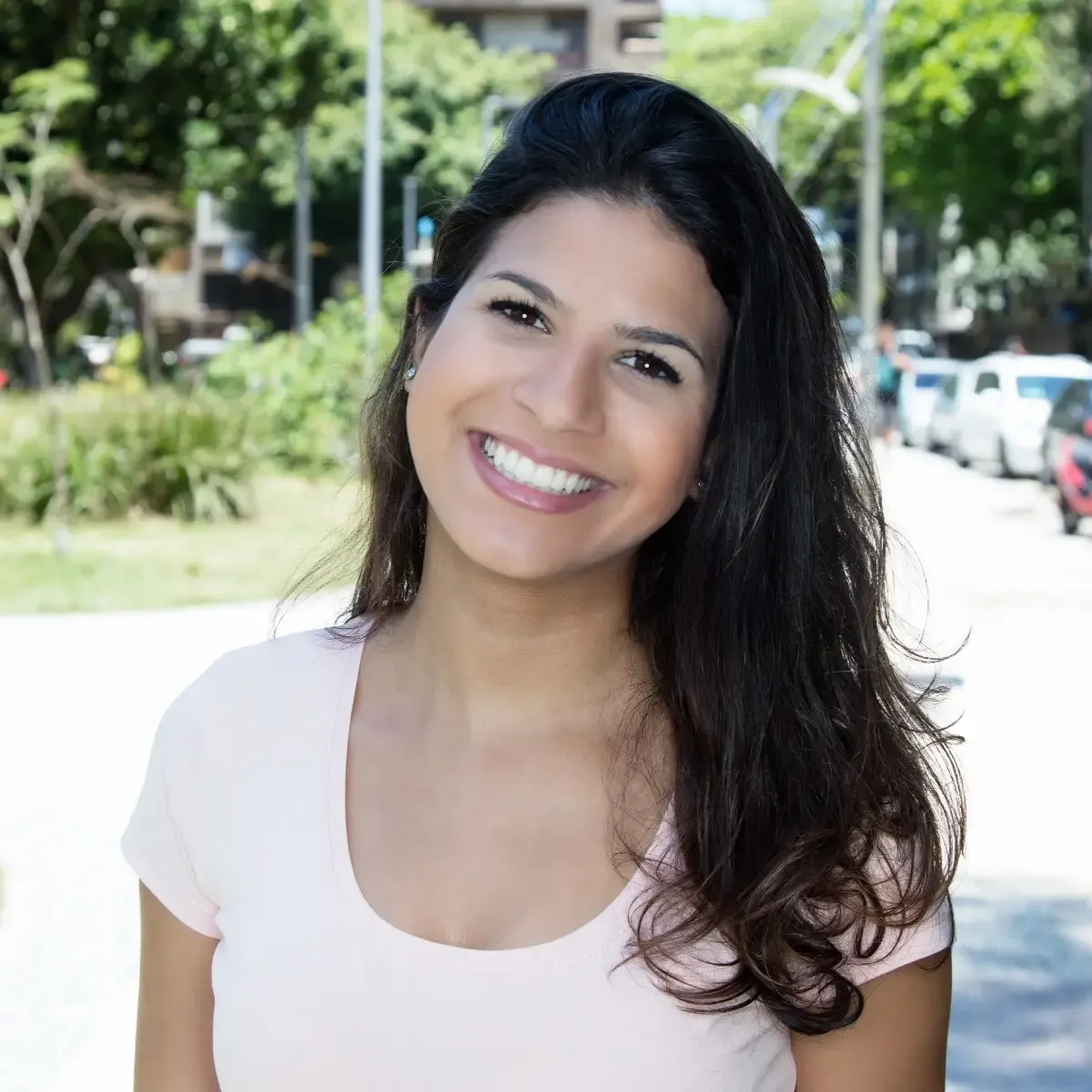 Mulher sorridente posa ao ar livre diante de árvores e vegetação desfocadas.
