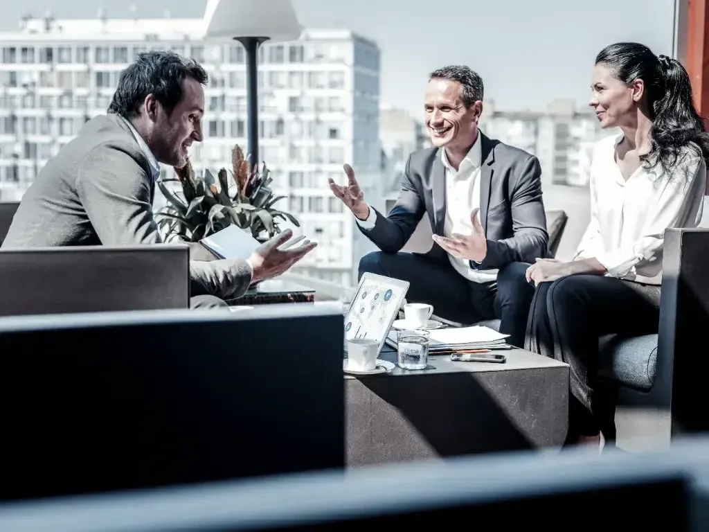 Grupo de profissionais conversa em sala corporativa, em fotografia preto e branco.