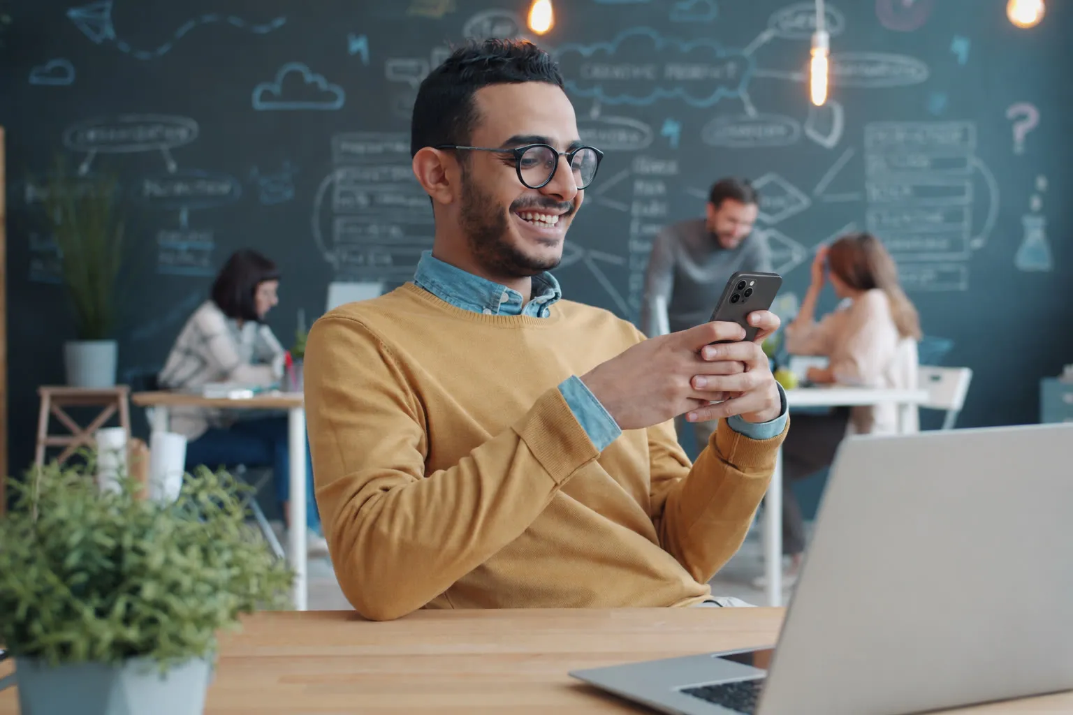 Empreendedor num escritório compartilhado, sorrindo ao ler a resposta no celular